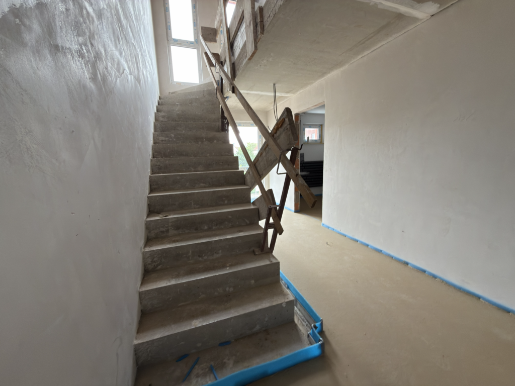 Baustellenaufnahme Treppenhaus im BV Lindhorst – Betontreppe im Ausbauzustand mit verputzten Wandflächen, Estrich und provisorischer Absturzsicherung.
