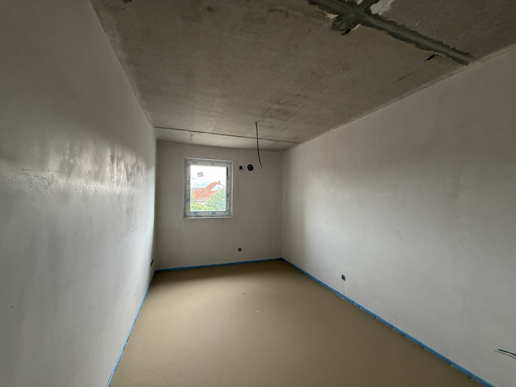 Baustellenaufnahme des Schlafzimmers einer 2-Zimmer-Wohnung in Lindhorst – verputzte Wandflächen, vorbereitete Elektroanschlüsse und fertiggestellter Estrichboden im Ausbauzustand.