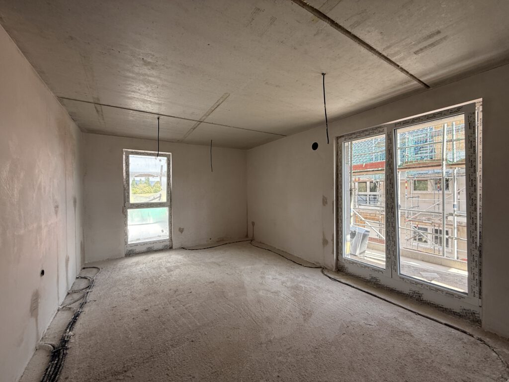 Wohnzimmer im Neubauprojekt Bad Oeynhausen während des Innenausbaus mit großen Fensterelementen und Zugang zum Außenbereich.