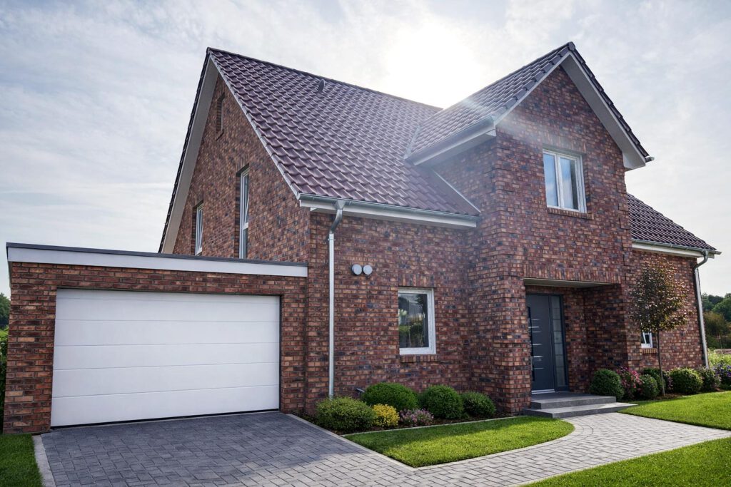 Frontansicht des Einfamilienhauses Classic 195 mit hochwertiger Klinkerfassade, integrierter Garage, überdachtem Eingang und Satteldach mit Terrassengiebel – klassisch-moderner Massivbau, Energieeffizienzklasse A+, Fertigstellung 2023