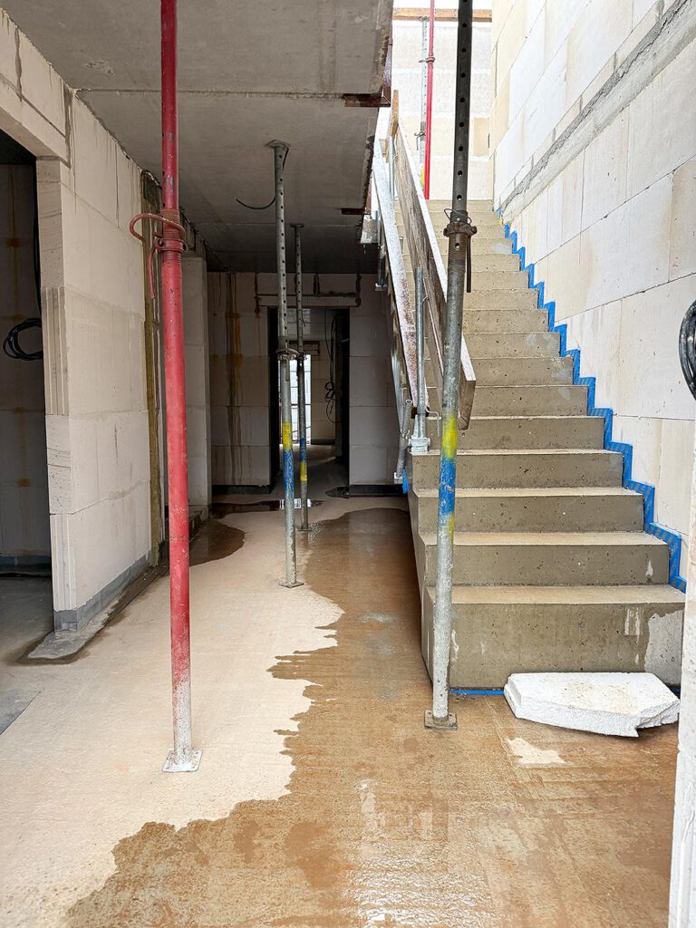 Baustellenaufnahme Treppenhaus am Zum Rehmer Eck in Bad Oeynhausen – Betontreppe im Rohbauzustand mit sichtbaren Installationsleitungen und Deckenstützen.