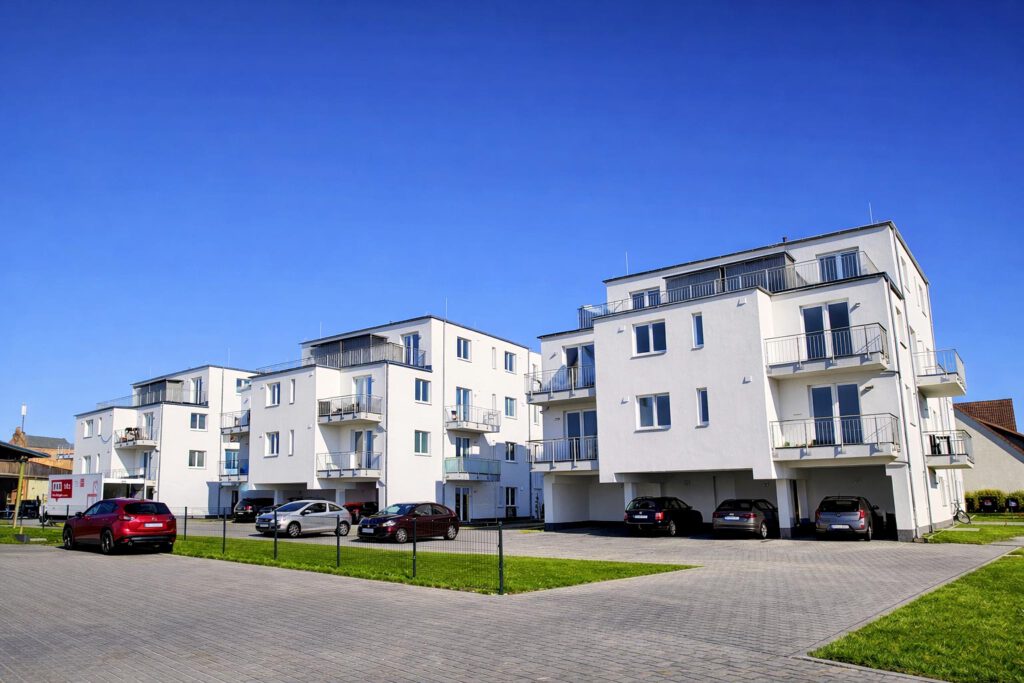 Außenansicht der drei modernen Mehrfamilienhäuser in Lehrte-Hämelerwald mit weißer Putzfassade, Balkonen und Parkplätzen – 54 geförderte Wohneinheiten, Fertigstellung 2024