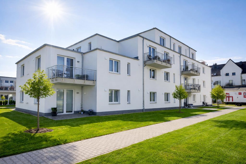 Gartenansicht eines Mehrfamilienhauses in Lehrte-Hämelerwald mit Balkonen, Erdgeschossterrassen und gepflegten Grünflächen – energieeffizienter Neubau mit Vinylboden und 3-fach-Verglasung