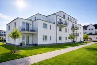 Gartenansicht eines Mehrfamilienhauses in Lehrte-Hämelerwald mit Balkonen, Erdgeschossterrassen und gepflegten Grünflächen – energieeffizienter Neubau mit Vinylboden und 3-fach-Verglasung