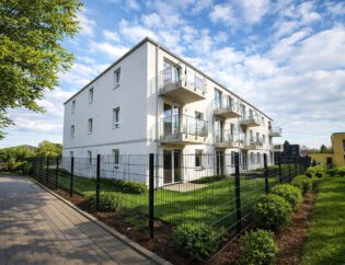 Außenansicht des Mehrfamilienhauses am Werbeker Ring in Pattensen mit weißer Putzfassade, Balkonen und gepflegten Grünanlagen – geförderter Neubau mit 24 Wohneinheiten, KfW-55-Standard, Fertigstellung 2026