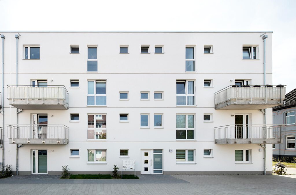 Frontansicht des Mehrfamilienhauses Peiner Straße 5 in Sehnde mit weißer Putzfassade, Hauseingang und Balkonen – geförderter Neubau mit 36 Zwei-Zimmer-Mietwohnungen, Energieeffizienzklasse A, Fertigstellung 2020