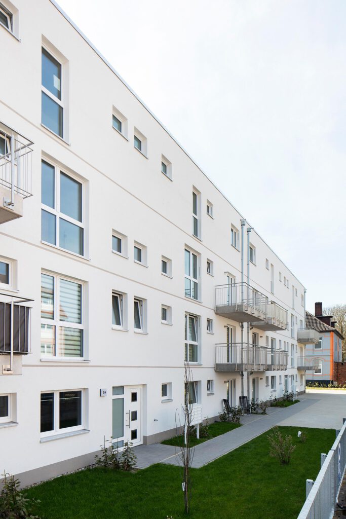 Seitenansicht des geförderten Mehrfamilienhauses Peiner Straße in Sehnde mit Hauseingang, Balkonen und Grünstreifen – zwei Baukörper mit insgesamt 36 Mietwohnungen, barrierearmer Zugang, Aufzug OTIS